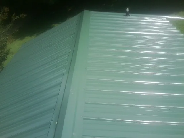 New green metal panels meeting at the ridge of a roof — Flat Roof Repair work by our crew in Petersburg