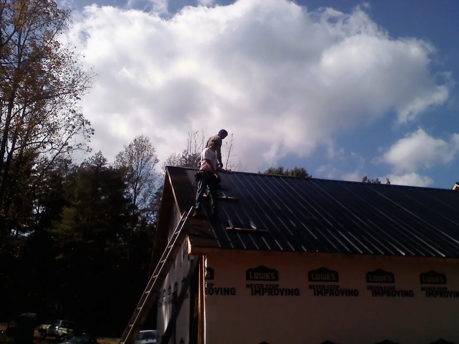 Roofer fastening dark metal panels high against a cloudy sky, from a Roof Inspection job in Petersburg